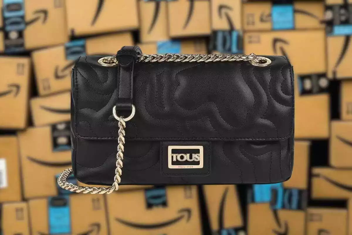 Fotomontaje con cajas de Amazon desenfocadas y delante bolso negro Tous con cadena dorada Fotomontaje con cajas de Amazon desenfocadas y delante bolso negro Tous con cadena dorada