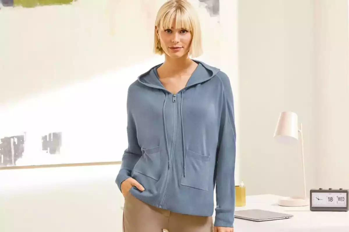 Mujer posando con una chaqueta azul con capucha y vemos parte de un pantalón beige Mujer posando con una chaqueta azul con capucha y vemos parte de un pantalón beige