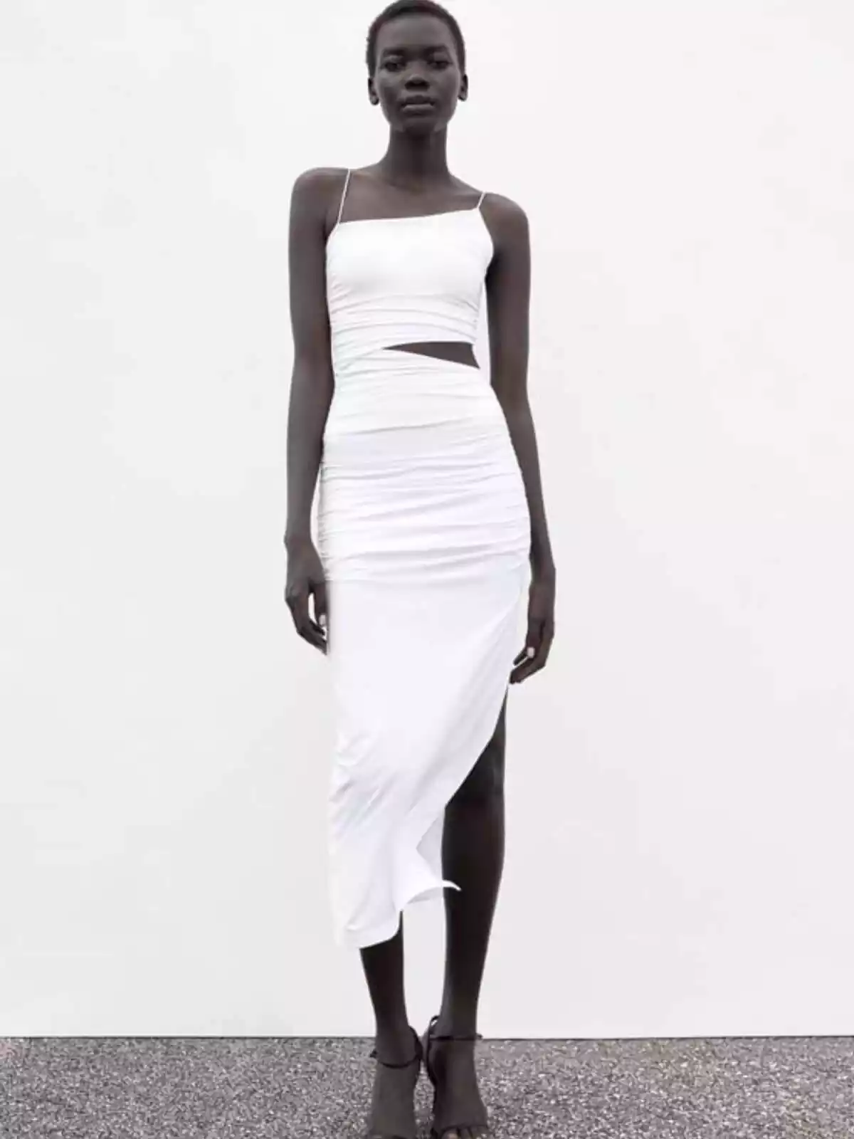 Modelo de Zara que lleva vestido blanco de la firma con detalle de obertura sobre fondo blanco y suelo gris Modelo de Zara que lleva vestido blanco de la firma con detalle de obertura sobre fondo blanco y suelo gris