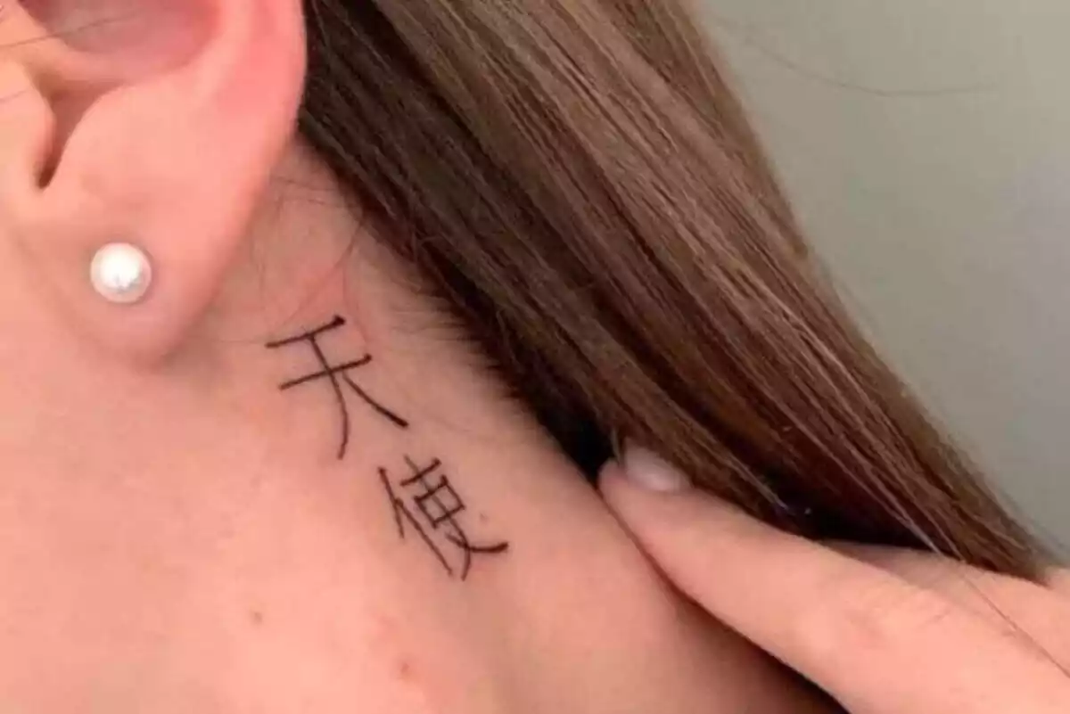 Foto detalle de una mujer retirándose el pelo de la nuca con un tatuaje de letras chinas Foto detalle de una mujer retirándose el pelo de la nuca con un tatuaje de letras chinas