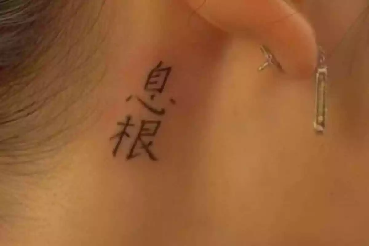 Foto detalle de un cuello femenino con un tatuaje pequeño de letras chinas y un pendiente de oro Foto detalle de un cuello femenino con un tatuaje pequeño de letras chinas y un pendiente de oro