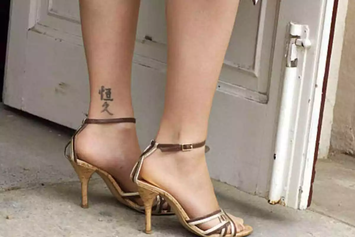 Foto detalle de unas piernas femeninas con zapatos de tacón y un tatuaje de letras chinas en el tobillo Foto detalle de unas piernas femeninas con zapatos de tacón y un tatuaje de letras chinas en el tobillo