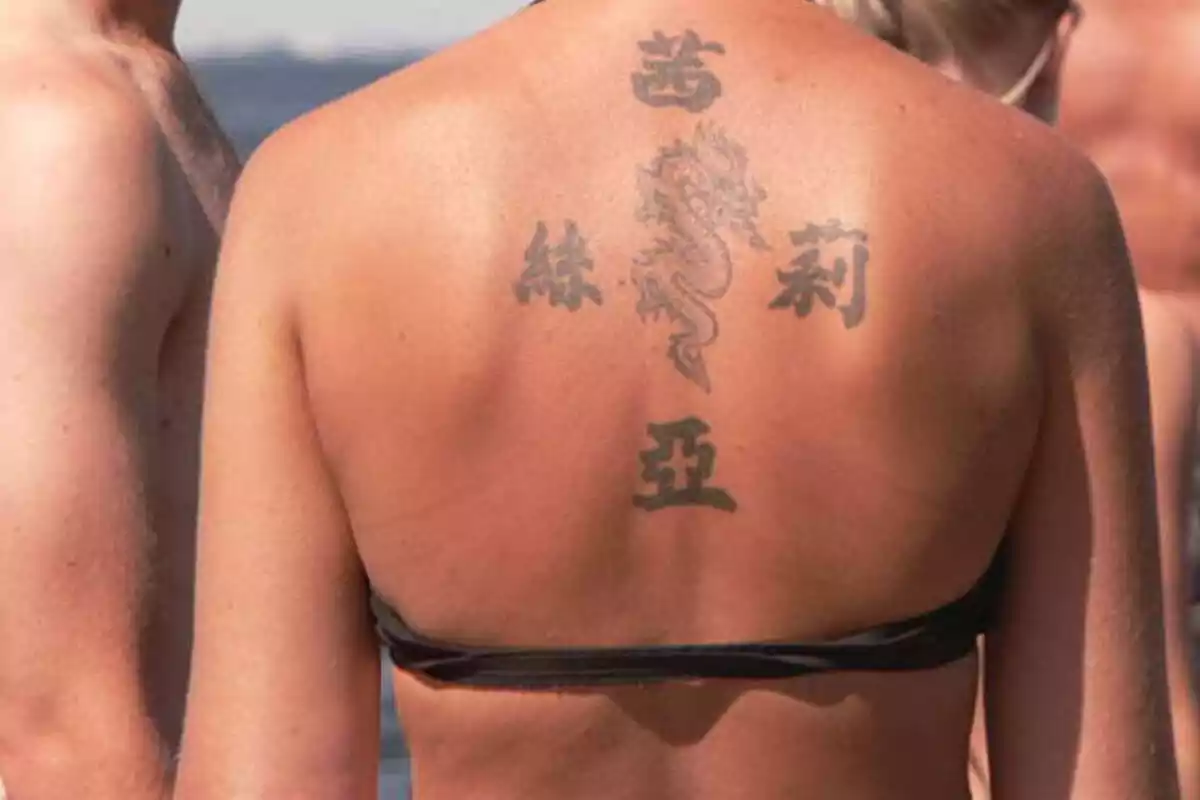 Foto de la espalda bronceada de una mujer en la playa con un tatuaje de letras chinas y un dragón en el centro Foto de la espalda bronceada de una mujer en la playa con un tatuaje de letras chinas y un dragón en el centro