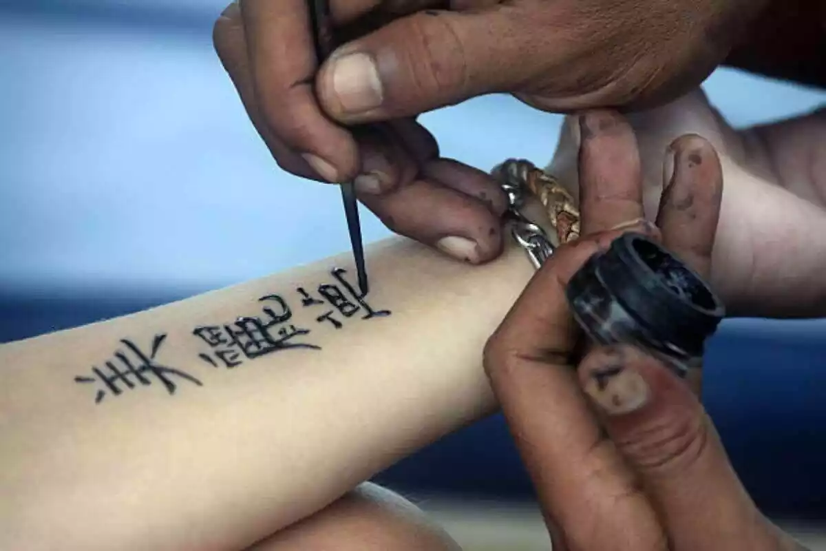 Foto detalle de un brazo siendo tatuado con tinta negra y con unas letras chinas Foto detalle de un brazo siendo tatuado con tinta negra y con unas letras chinas