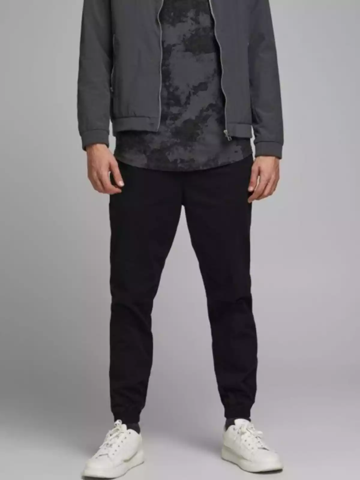 Aparece la parte inferior de un hombre, con pantalones oscuros y deportivas blancas Aparece la parte inferior de un hombre, con pantalones oscuros y deportivas blancas