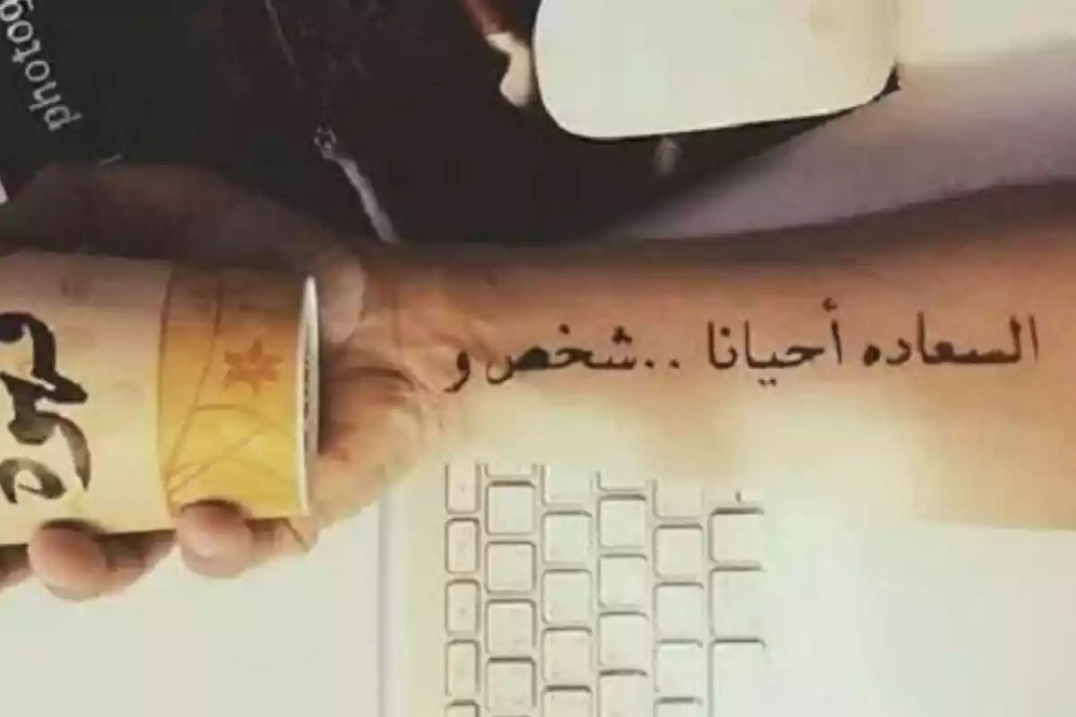 Foto detalle de un brazo que sujeta un vaso apoyado sobre un teclado con un tatuaje en letras árabes Foto detalle de un brazo que sujeta un vaso apoyado sobre un teclado con un tatuaje en letras árabes