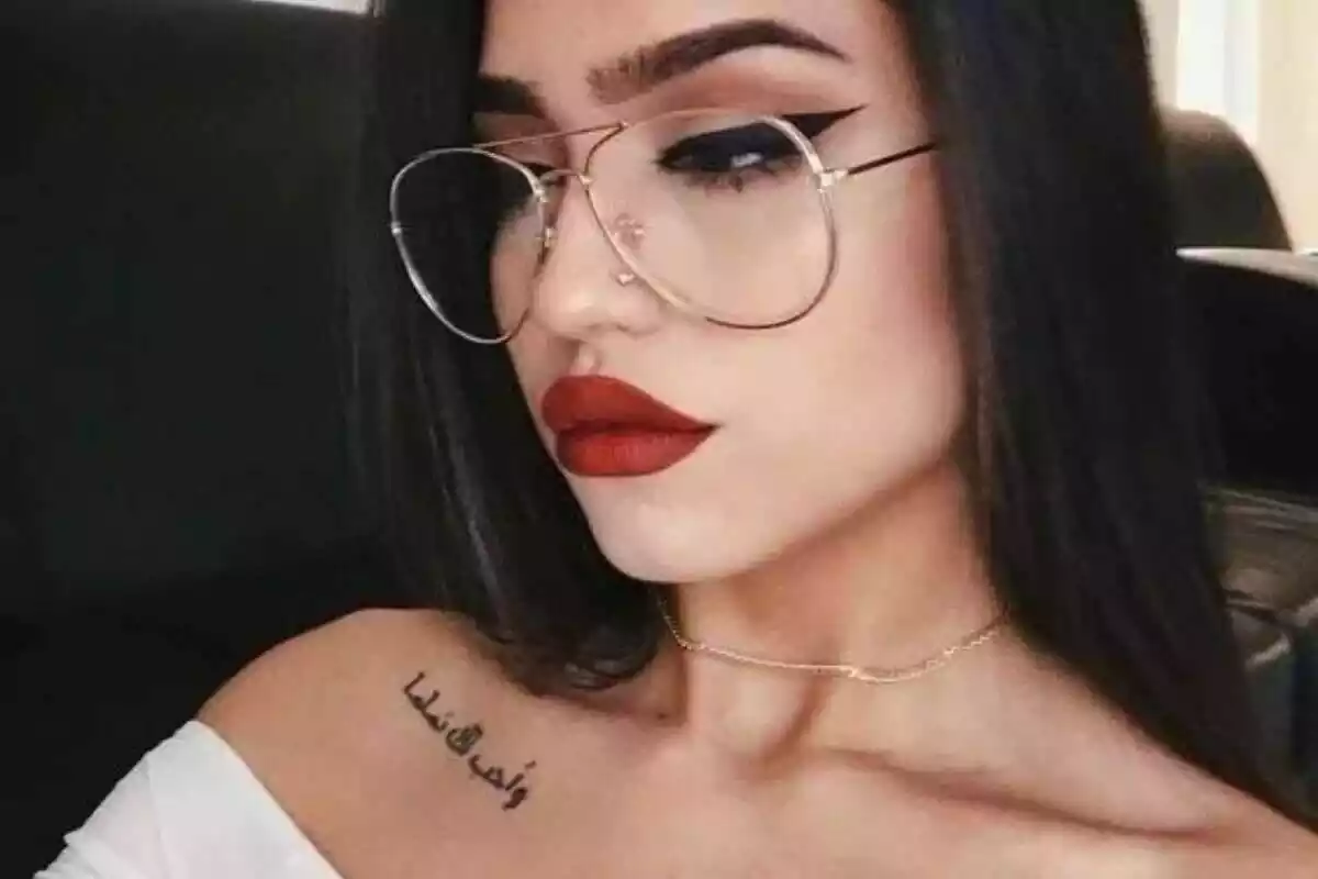 Foto de una mujer joven con gafas que luce un tatuaje de letras árabes en el hombro Foto de una mujer joven con gafas que luce un tatuaje de letras árabes en el hombro