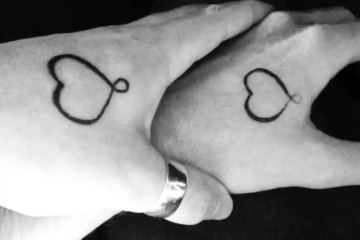 Foto detalle de unas manos unidas que tienen el mismo tatuaje de un corazón formando el símbolo del infinito Foto detalle de unas manos unidas que tienen el mismo tatuaje de un corazón formando el símbolo del infinito