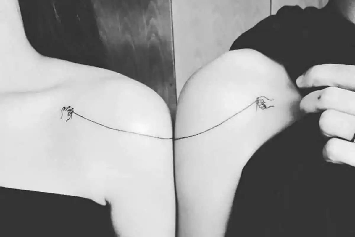 Foto detalle de una pareja de hombros pegados y unidos por un tatuaje en el que unas manos sujetan un hilo Foto detalle de una pareja de hombros pegados y unidos por un tatuaje en el que unas manos sujetan un hilo