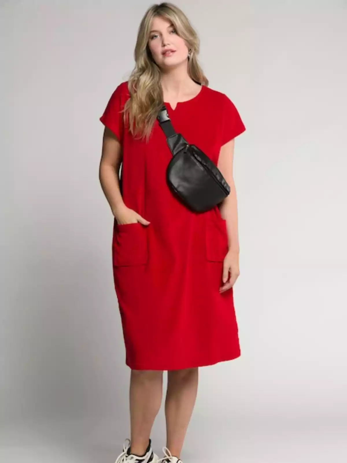 Mujer con un vestido rojo, deportivas blancas y un bolso bandolera negro que le cruza el pecho Mujer con un vestido rojo, deportivas blancas y un bolso bandolera negro que le cruza el pecho