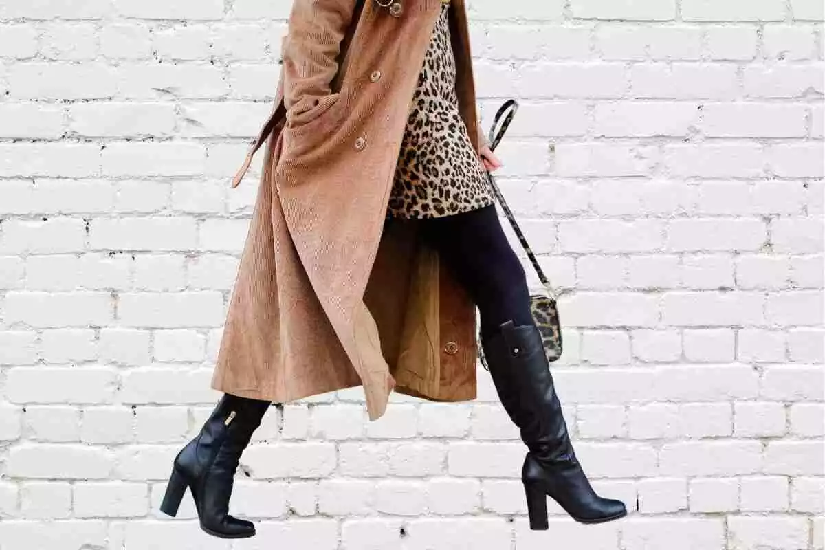 mujer con botas altas negras, medias negras, vestido de leopardo y un abrigo marrón